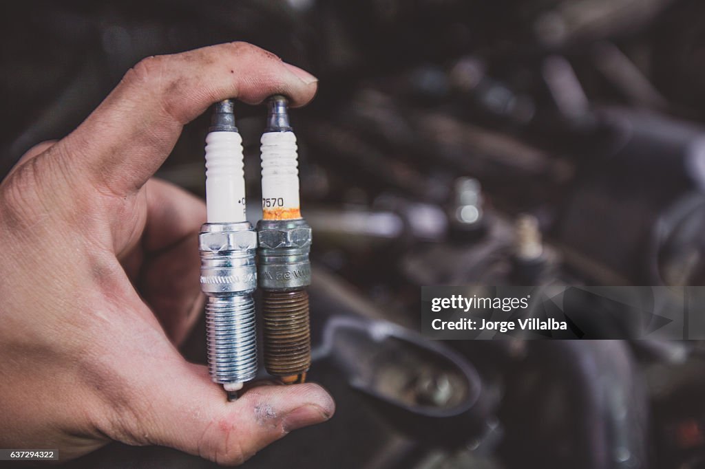 Holding old and new car spark plugs on engine