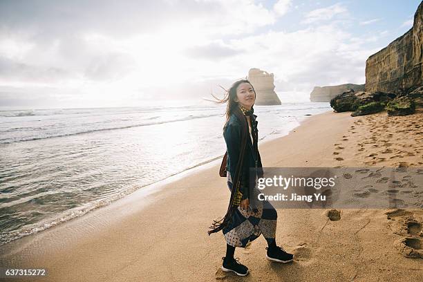 a woman is walking on beach while looking to camera with smile - melbourne australië stockfoto's en -beelden