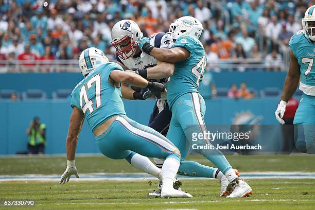 Spencer Paysinger and Kiko Alanso of the Miami Dolphins tackle Matt Lengel of the New England Patriots on January 1, 2017 at Hard Rock Stadium in...