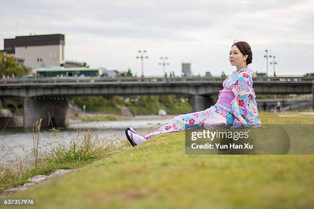 girl in kimono sitting on river bank in kyoto - kamo river stock pictures, royalty-free photos & images