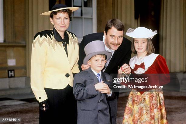 Formula One driver Nigel Mansell shows off his OBE outside Buckingham Palace, with the help of his wife Roseanne and their children Leo and Chloe
