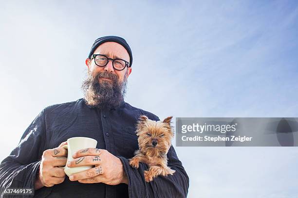 bearded man holding small dog and coffee cup - stil stock-fotos und bilder
