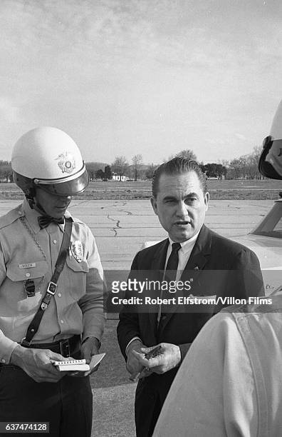 American politician George Wallace stands with two motorcycle police officers on the tarmac at an unidentified airport, Alabama, 1968. Wallace was in...