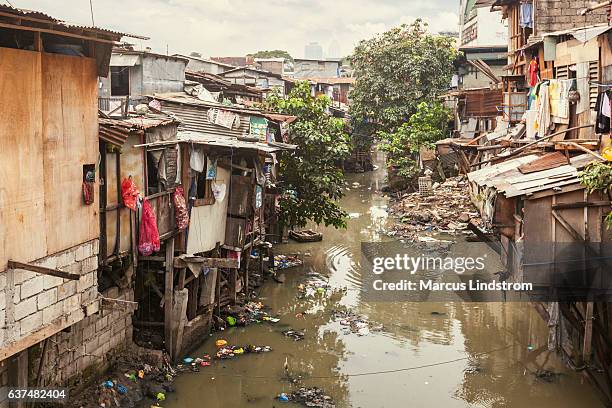 baracche lungo un canale inquinato - povertà foto e immagini stock