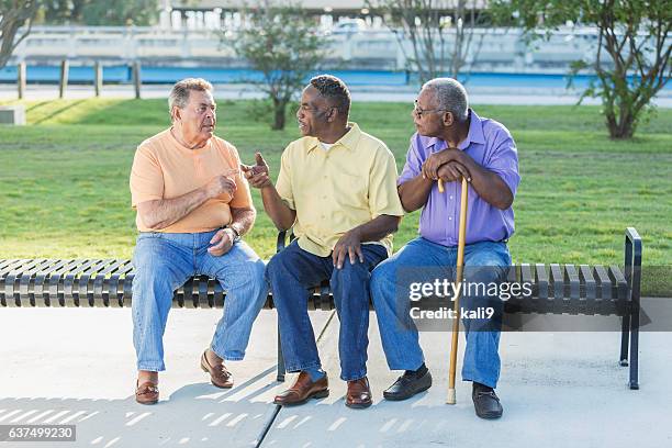 three multi-ethnic senior men sitting on bench talking - friends serious stock pictures, royalty-free photos & images