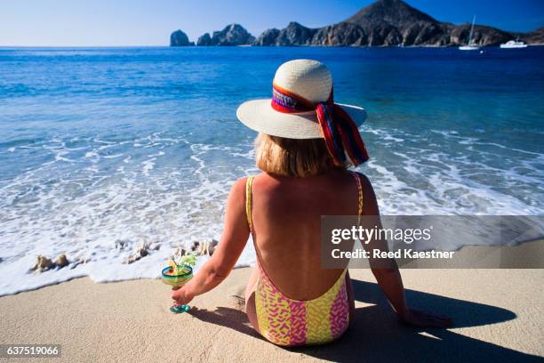 a tourist sits at the beach in cabo san lucas with a drink in hand watching the waves come in. - margarita beach stock-fotos und bilder