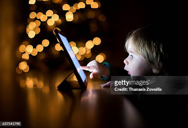 2 year old boy using a digital tablet in the dark - bambino curioso foto e immagini stock