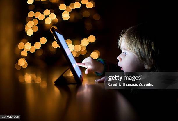 2 year old boy using a digital tablet in the dark - technology curiosity stock pictures, royalty-free photos & images