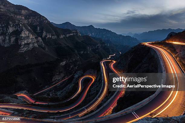 winding road with hairpin bends up the rocky mountain at dusk with traffic lights - winding road mountain stock pictures, royalty-free photos & images