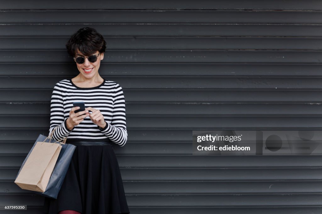 Frau schaut auf Handy mit Einkaufstaschen