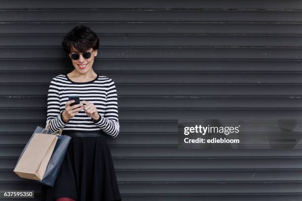 woman looking at mobile phone with shopping bags - happy consumer on phone stock pictures, royalty-free photos & images