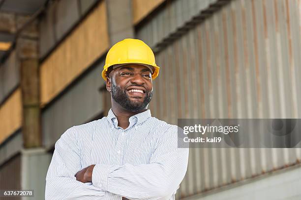 african american man wearing hard hat in warehouse - protective headwear stock pictures, royalty-free photos & images