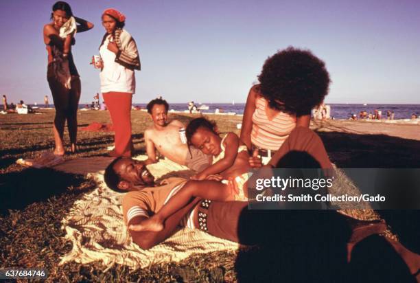 As the afternoon sun fades into evening, a family enjoys the 12th street beach on Lake Michigan, with two men lying town beside a woman and young...