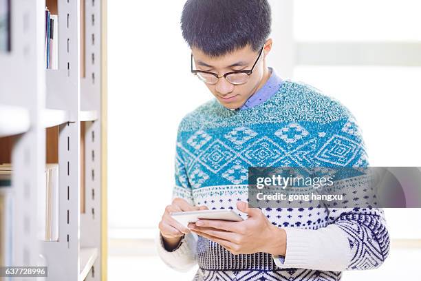 young asian man holds tablet in library - university asian students international portrait stock pictures, royalty-free photos & images