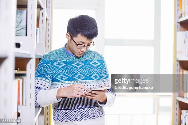 young asian man holds tablet in library - university asian students international portrait stock pictures, royalty-free photos & images