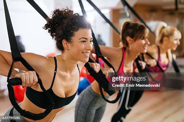 women doing arm exercises with suspension straps at gym. - suspension training stock pictures, royalty-free photos & images