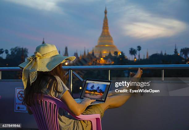 Tourist woman is watching the famous Shwedagon, or Shwedagon-Paya pagoda while working with a notebook and internet, making telephone calls or writes...