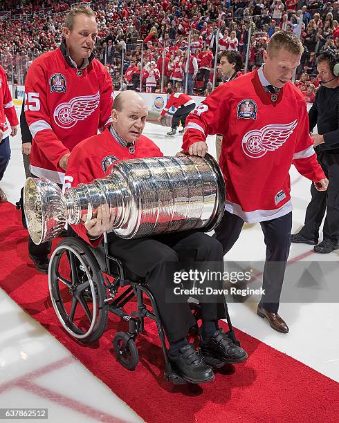 Vladimir Konstantinov holds the Stanley Cup as former teammates Darren McCarty and Kris Draper help him off the ice after the ceremony for the...