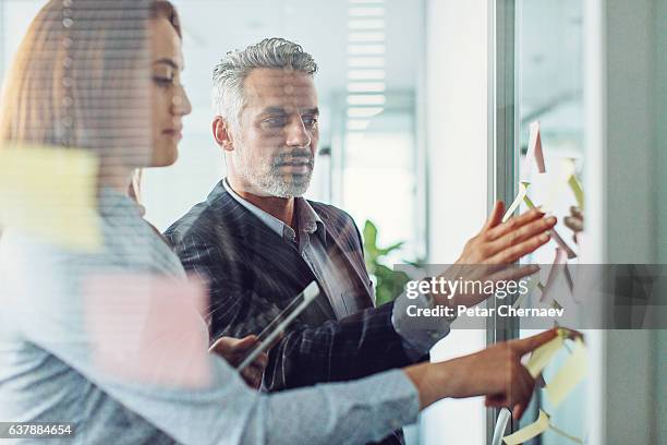 analysieren der geschäftsstrategie - team looking at adhesive notes in board room during meeting stock-fotos und bilder