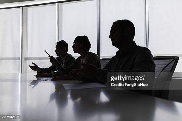 silhouette of business people negotiating at meeting table - fluisteren stockfoto's en -beelden
