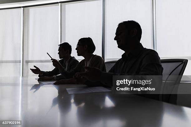 silhouette of business people negotiating at meeting table - ominous stock pictures, royalty-free photos & images