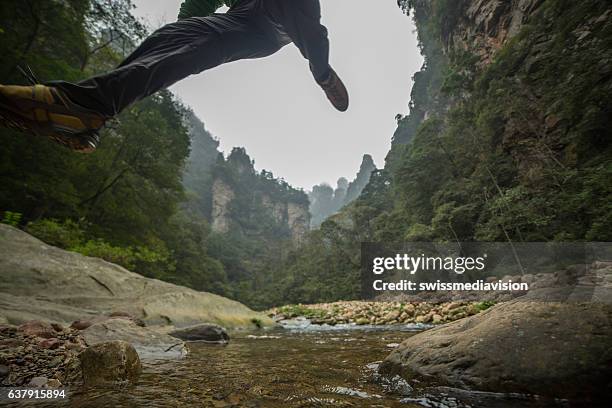 young man hiking jumps over the mountain river - quartz sandstone stock pictures, royalty-free photos & images