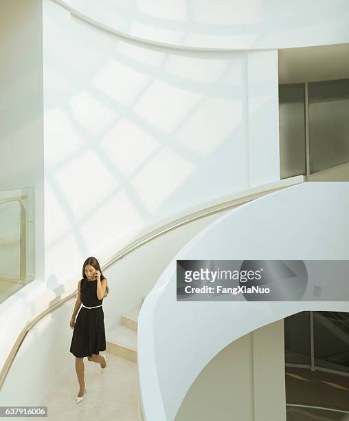 woman on phone descending staircase in modern building - architecture woman stockfoto's en -beelden