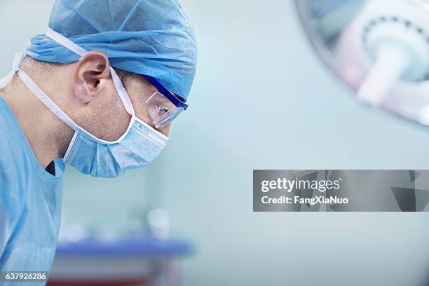 doctor looking down at patient in hospital operating room - surgical mask man stock pictures, royalty-free photos & images