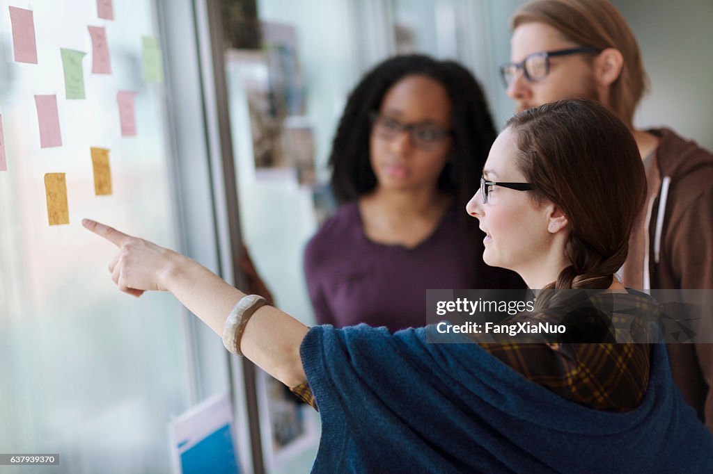 Creative colleagues reviewing ideas on wall in studio office