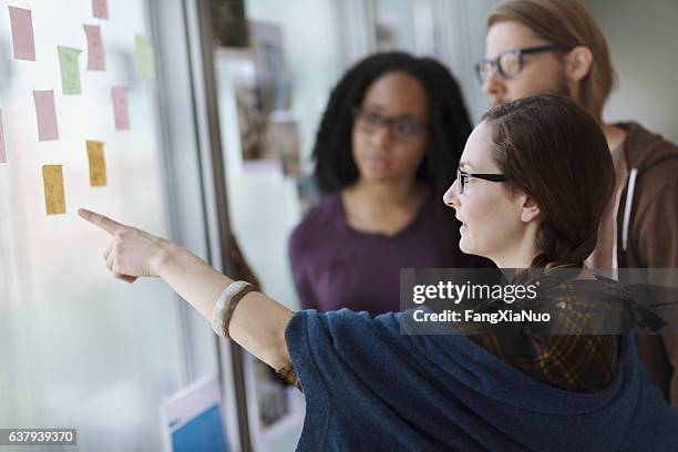 creative colleagues reviewing ideas on wall in studio office - politica e governo imagens e fotografias de stock