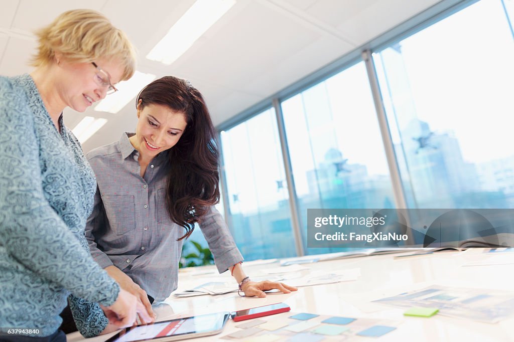 Women reviewing plans on tablet computer in studio