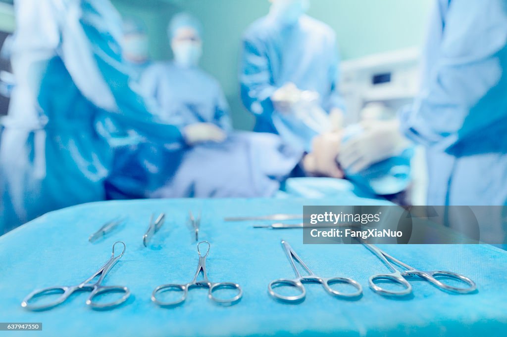 Ferramentas cirúrgicas dispostas em bandeja com médicos na sala de cirurgia