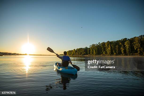 an adult male is kayaking at sunset on a peaceful - kano stockfoto's en -beelden