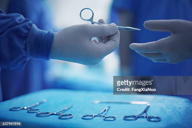 ärzte passieren chirurgische werkzeuge im operationssaal des krankenhauses - ablagekasten stock-fotos und bilder