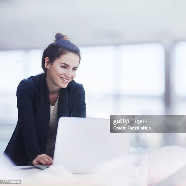 woman working on laptop in bright office - helder stockfoto's en -beelden