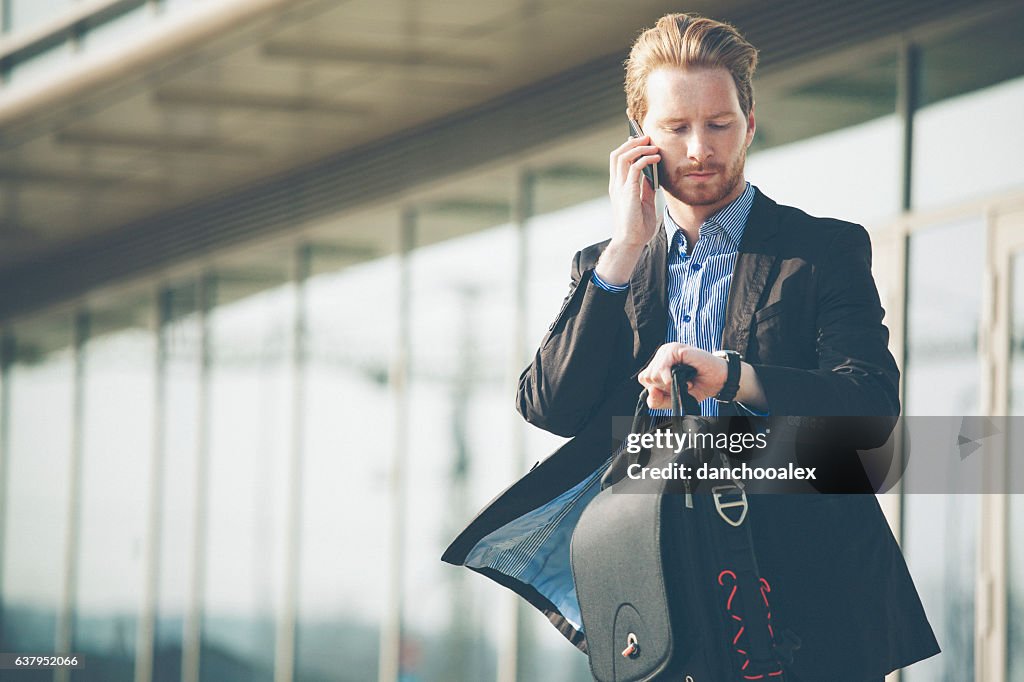Young businessman checking time and talking on the cell phone