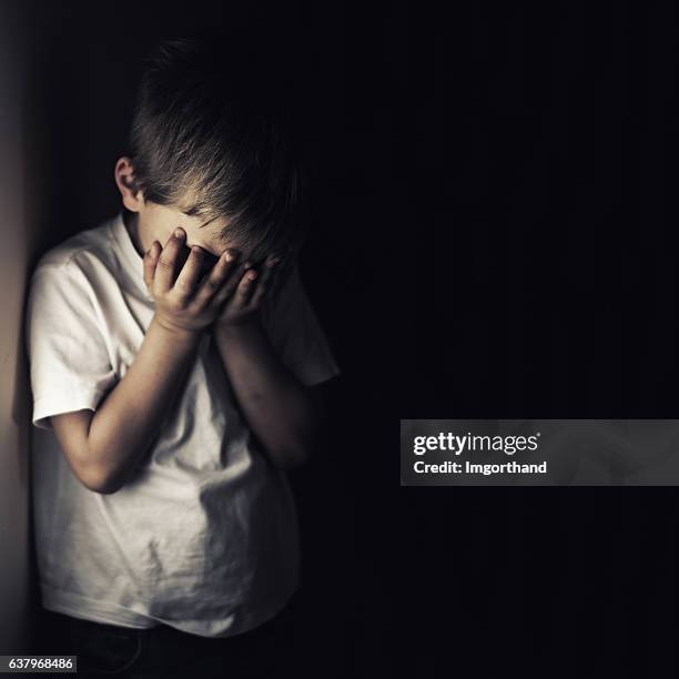 depressiv weinender kleiner junge, der den kopf in den händen hält - missbrauch stock-fotos und bilder