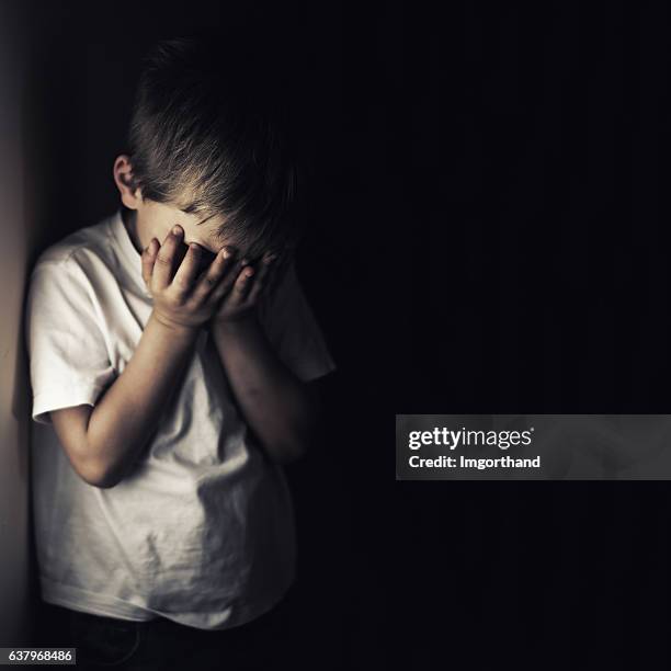 depressed crying little boy holding head in hands - kindermishandeling stockfoto's en -beelden