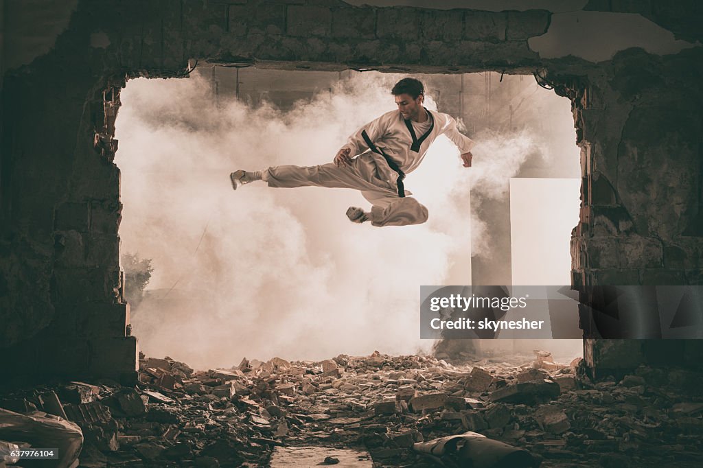 Skilful black belt martial artist performing fly kick.