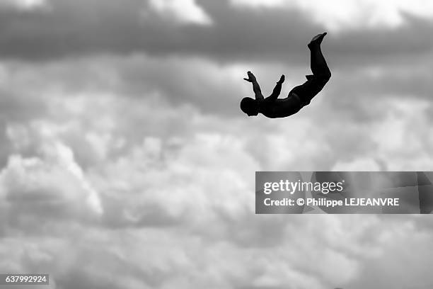 silhouette of a man doing a swallow dive against clouds - diving risk stock-fotos und bilder