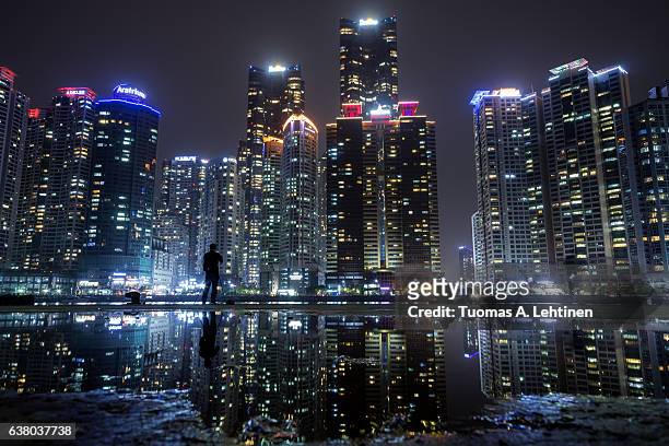 view of skyscrapers at the marine city residential area in haeundae district and their reflection in a puddle in busan, south korea, at night. - busan fotografías e imágenes de stock
