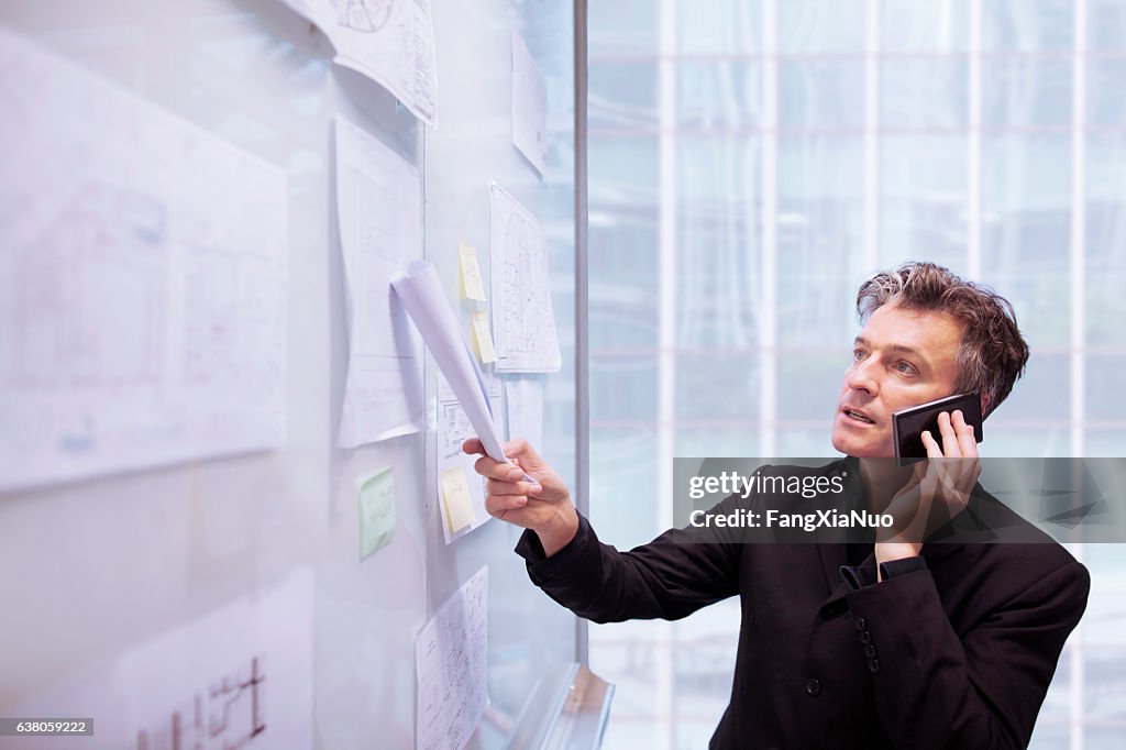 Architect designer using phone pointing to plans on wall