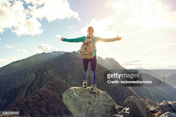 giovane donna escursionismo in montagna raggiunge la cima, outstretches le braccia - vetta foto e immagini stock