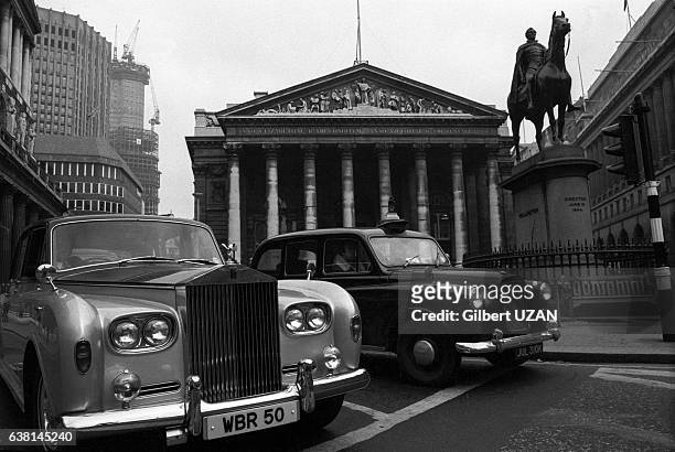 Une Rolls-Royce et un taxi anglais devant la bourse de Londres en novembre 1976, à Londres, Royaume-Uni.