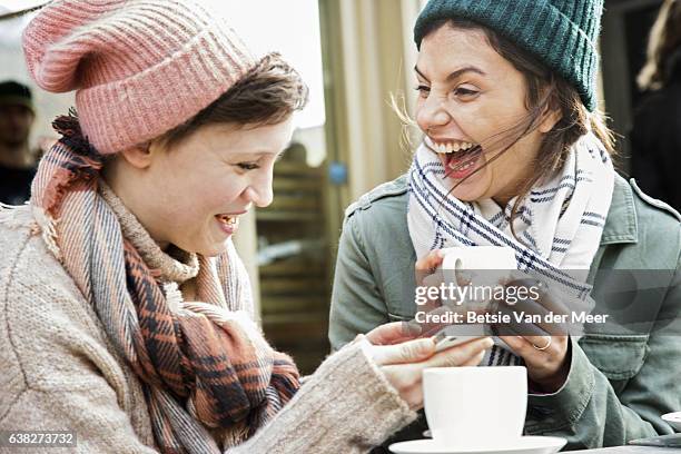 two female friends laughing, drinking tea, in outside urban foodmarket cafe, in autumn time. - tea outdoor stock-fotos und bilder