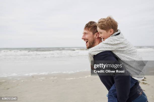 happy father carrying son piggyback on the beach - boy jeans stockfoto's en -beelden