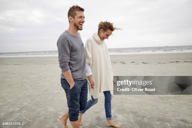 happy couple walking on the beach - gray jeans stock-fotos und bilder