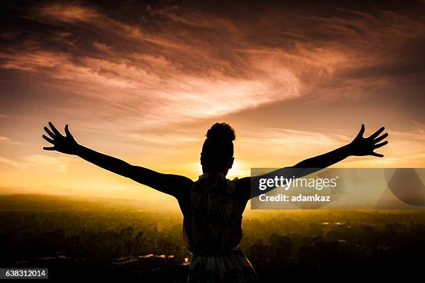 african american woman raising arms at sunset - bidden stockfoto's en -beelden