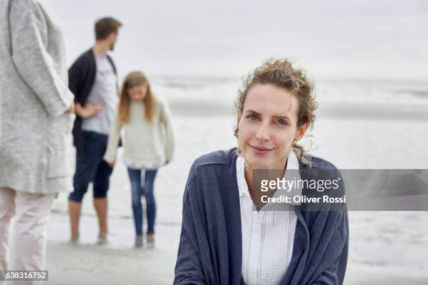 smiling woman on the beach with family in background - curly hair woman white shirt stock pictures, royalty-free photos & images