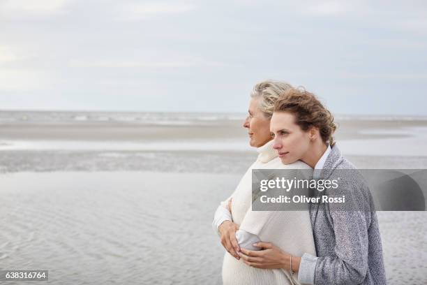 adult daughter hugging mother on the beach - mother daughter beach stock pictures, royalty-free photos & images